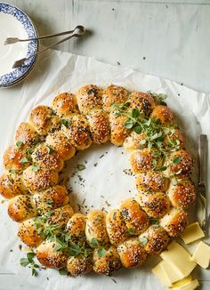 a bread wreath with cheese and herbs on it next to a knife, fork and spoon