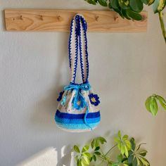 a crocheted bag hanging from a wooden hook on a wall next to a potted plant