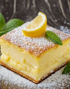 a piece of lemon cake with powdered sugar on top and mint leaves around it