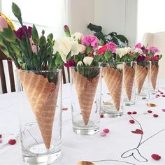 four ice cream cones with flowers in them on a white tableclothed table cloth