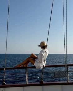 a woman sitting on the back of a boat looking out at the ocean while wearing a hat