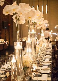 a long table is set with white flowers and candles in tall vases on each side