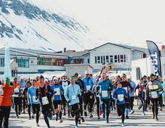 a large group of people running down a street with snow covered mountains in the background