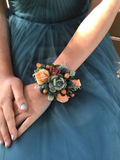 a close up of a person wearing a dress and holding a flower bracelet with succulents on it