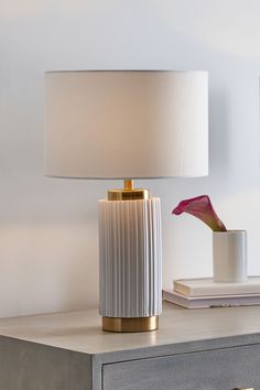 Simple and Elegant. This column ceramic table lamp is finished with a ridged detailing and white colourway. Encased top and bottom with a contrasting gold metal and finished with a faux cotton self lined white shade for ultimate understated glamour. Also available in other colours. Wipe clean only. 90% Ceramic, 5% Cotton, 5% PVC. Cool Bedside Lamps, Gold And White Lamp, Neutral Aesthetic Home Decor, Bedroom Side Table Lamps, Grey Lamps, Bachelorette House, Minimal Table Lamp, Bed Side Table Lamp, Bedroom Lamps Bedside