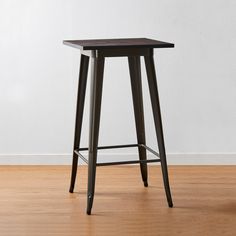 a black wooden stool sitting on top of a hard wood floor next to a white wall