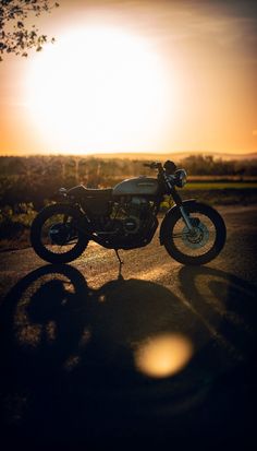 the motorcycle is parked on the side of the road in the sun setting behind it