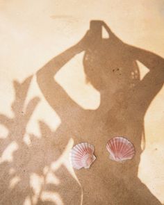 a woman standing next to two seashells on top of a sandy beach with her arms behind her head