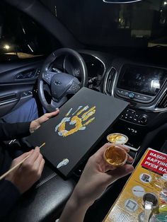 two people holding drinks in their hands while sitting in the driver's seat of a car