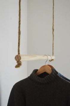 a sweater hanging from a wooden hanger on a white wall next to a black shirt