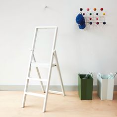 a white ladder leaning against a wall next to a trash can and bucket on the floor