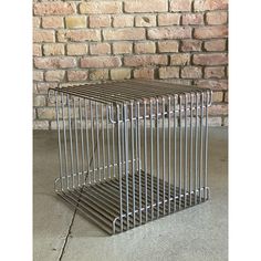 a metal birdcage sitting on top of a cement floor next to a brick wall