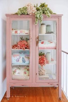 an old china cabinet painted pink with flowers on the top and glass doors that are open