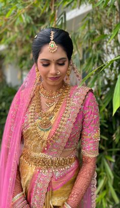 a woman in a pink and gold bridal outfit with jewelry on her neck, standing outside