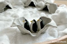 three little penguins in an egg carton on some fluffy white material with rocks and snow around them