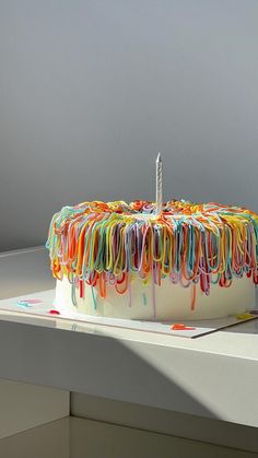 a birthday cake decorated with multicolored icing and a single candle on top