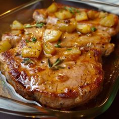 two pieces of meat with potatoes and herbs on it in a glass dish sitting on a wooden table