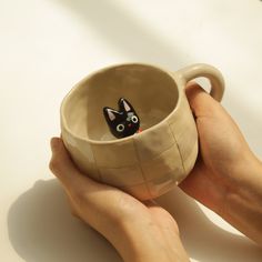 a person holding a coffee cup with a cat figurine in the middle of it