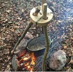 an open fire pit with a pot on it in the middle of leaves and rocks