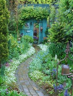 a garden with flowers, plants and a path leading to a blue door in the background