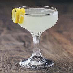 a glass filled with a white liquid and a lemon slice on the rim, sitting on top of a wooden table