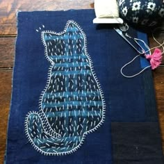 a blue piece of cloth with a cat on it next to some scissors and thread