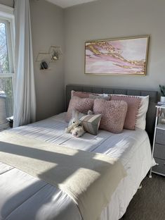 a bed with pink and white pillows in a bedroom next to a painting on the wall