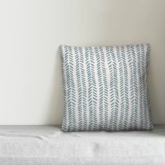 a blue and white pillow sitting on top of a couch next to a wall with a plant