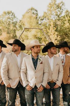 a group of men standing next to each other wearing cowboy hats and suits with trees in the background