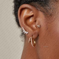 a close up view of a woman's ear with three diamond hoops