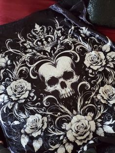 a black and white skull with roses on it's hoodie is sitting on a red blanket