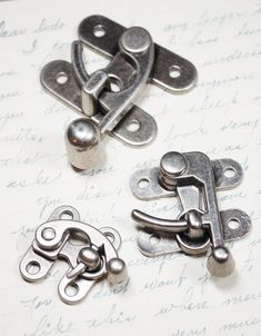 three metal latches on top of a piece of paper with writing in the background