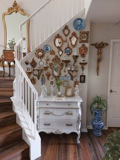 a white dresser sitting under a stair case next to a wall with pictures on it