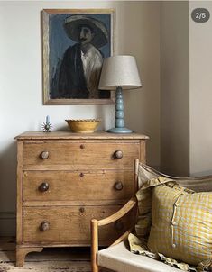 an old dresser with a painting on it next to a chair and lamp in a room