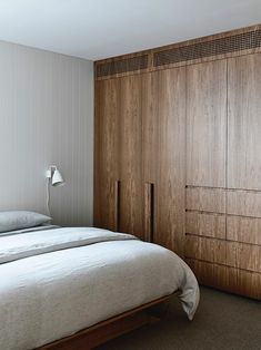 a bed sitting next to a wooden closet in a bedroom on top of a carpeted floor