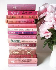 a stack of books sitting on top of a table next to a vase filled with flowers