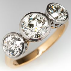 three stone diamond ring in yellow gold and white gold with diamonds on the sides, set against a grey background