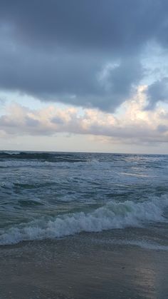 the ocean waves are rolling in to shore on a cloudy day with blue sky and white clouds