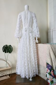 Stunning True Vintage white maxi dress from Finnish designer Kaisu Heikkilä from the 1970s. White flowy fabric with generous dreamy net lace floral decorations all over. Queen Anne neckline. Wide puff sleeves with elasticated cuffs. Sewn on tie belt for a great fit and a beautiful bow in the back. Lined, except for the sleeves. Zipper in the back. Made in Finland! BRAND: Heikkilä ERA: 1970s COLOR: White Fabric: No fabric tag, but it`s for sure a synthetic SIZE: Vintage size 36, fits best modern White Lace Patchwork Maxi Dress For Party, White Lace Maxi Dress With Lace Patchwork, White Lace Patchwork Maxi Dress For Wedding, Spring Maxi Dress With Lace Sleeves And Floor-length, Spring Floor-length Maxi Dress With Lace Sleeves, White Lace Maxi Dress With Lace Sleeves, White Maxi Dress With Lace Sleeves, Vintage White Maxi Dress For Spring, White Maxi Dress With Lace Sleeves For Party