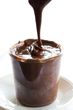 a chocolate dessert in a glass on a white plate with a spoon sticking out of it