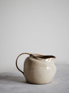 a white ceramic pitcher sitting on top of a marble countertop next to a wall