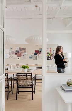 a woman standing in an office looking out the window at her work space and desks