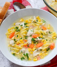 a white bowl filled with chicken noodle soup next to a red and white napkin