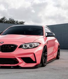 a pink bmw car parked in front of a building on a parking lot with other cars behind it