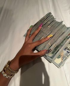 a person's hand with nails on top of stacks of cash and money notes