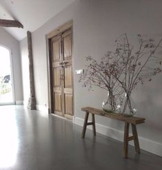 a vase with flowers on a table in front of an open door and wooden bench