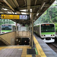 two green and white trains parked at a train station next to an escalator