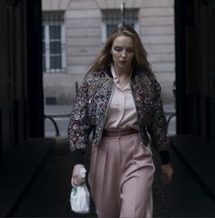 a woman is walking down the street with a handbag in her other hand while wearing a jacket and pants