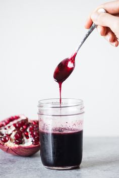 someone is pouring red liquid into a jar with pomegranate on the side