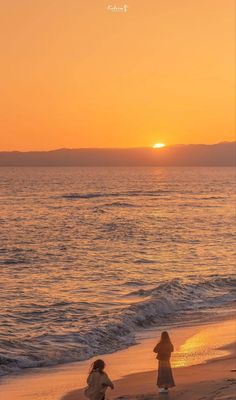 two people walking on the beach at sunset